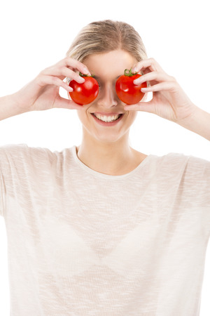Beautiful girl smiling and holding red tomatoes in front of the eyes, isolated over a white backgroundの写真素材