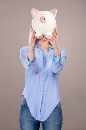Beautiful and attractive blonde woman holding a piggy bank in front of her headの写真素材