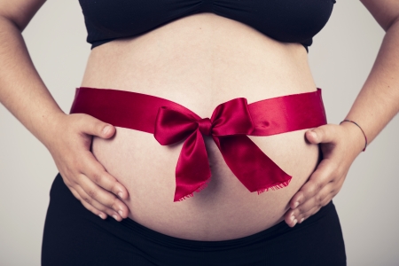 Pregnant woman showing her beautiful belly with a red lace, over a gray backgroundの写真素材