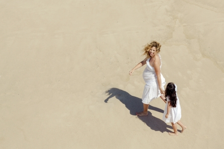 Beautiful pregnant woman and her little daughter walking on the beachの写真素材
