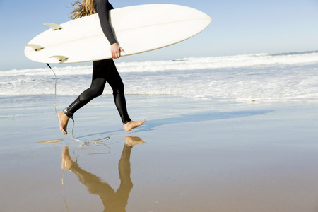 Teenage girl running on the beach with her surfboardの写真素材