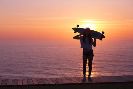 Beautiful girl holding a skateboard with the sunset in the backgroundの写真素材