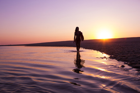Beautiful surfer girl walking in the beach with her surfboard at sunset