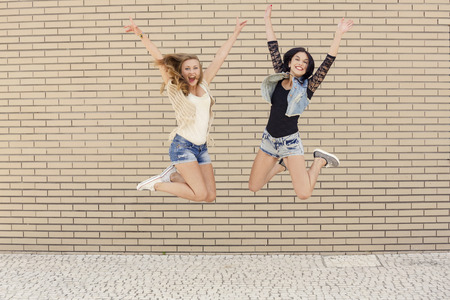 Two beautiful and young jumping in front of a brick wallの写真素材