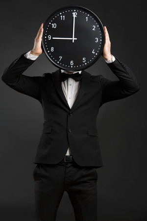 Handsome young man wearing a tuxedo and holding a clockの写真素材