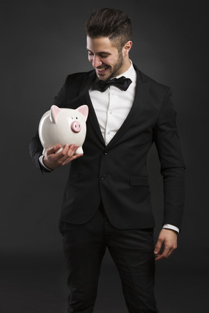 Man in tuxedo holding a pig money boxの写真素材