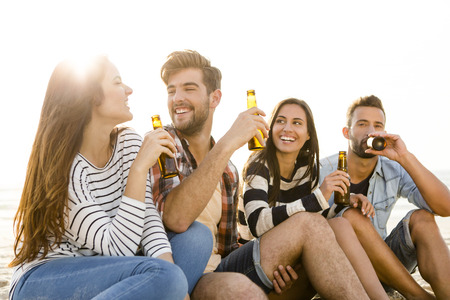 Friends having fun together at the beach and drinking a cold beer