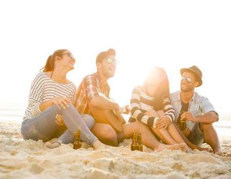 Friends having fun together at the beach, playing guitar and drinking beerの写真素材