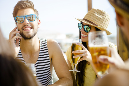 Friends having fun and drinking a cold beer at the beach barの写真素材