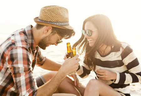 Young couple at the beach having fun, laughing and drinking beerの写真素材