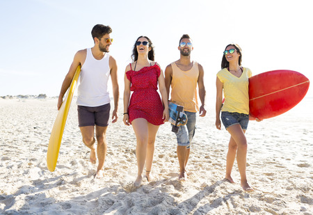 Group of friends walking together at the beach and holding surfboardsの写真素材