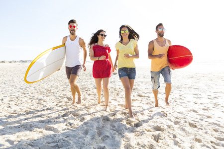 Group of friends walking together at the beach and holding surfboards