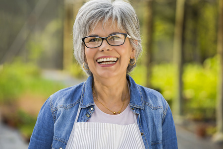 Beautiful mature woman working in a greenhouse, looking at camera while laughingの写真素材
