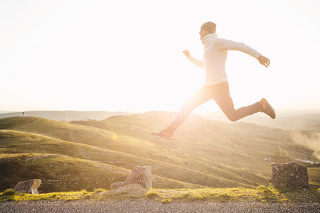 Man jumping over precipice between two stones on mountains at sunset