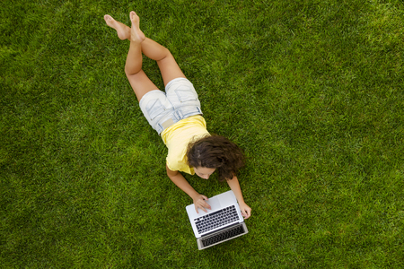 Beautiful young woman lying on the grass and working with a laptopの写真素材