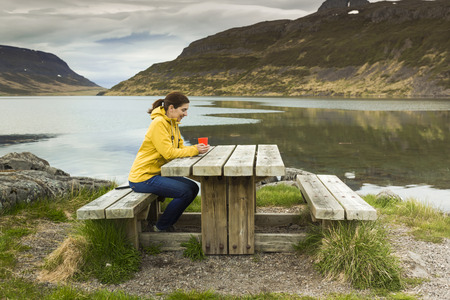 Beautiful woman resting close to a beautiful lake and drinkign a teaの写真素材