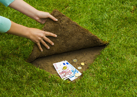 Finances concept, hands hiding money under the grassの写真素材
