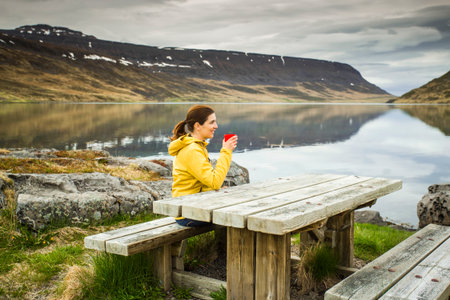 Beautiful woman resting close to a beautiful lake and drinkign a teaの写真素材