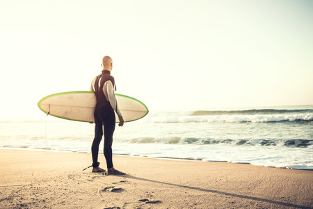Surfer on the beach holding is surfboaerd and watching the wavesの写真素材
