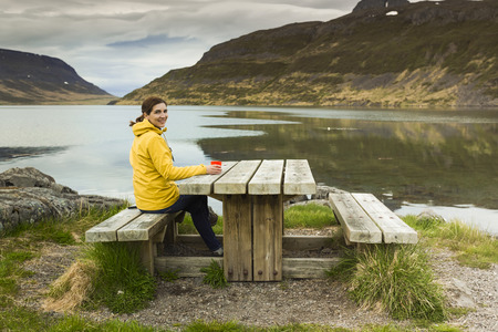 Beautiful woman resting close to a beautiful lake and drinkign a teaの写真素材
