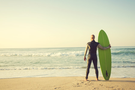 Surfer on the beach holding is surfboaerd and watching the waves