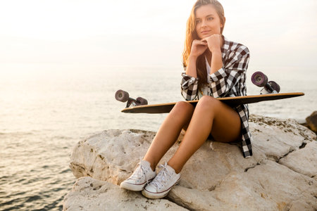 Beautiful and fashion young woman posing at the sunset with a skateboard