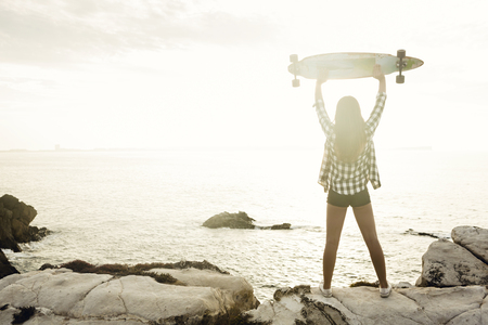 Beautiful and fashion young woman posing at the sunset with a skateboardの写真素材