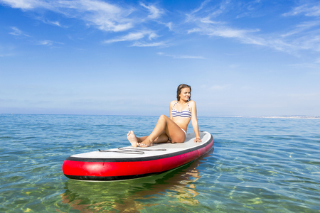 A beautiful woman sitting over a paddle surfboard and relaxing on a beautiful sunny dayの写真素材