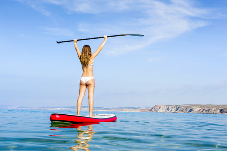 A beautiful and happy woman with arms up and learning paddle-surfの写真素材