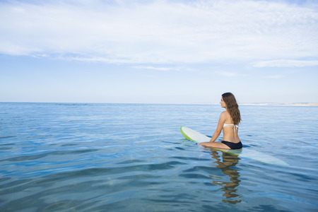 Beautiful young woman sitting on the surfboard and waiting for the waves