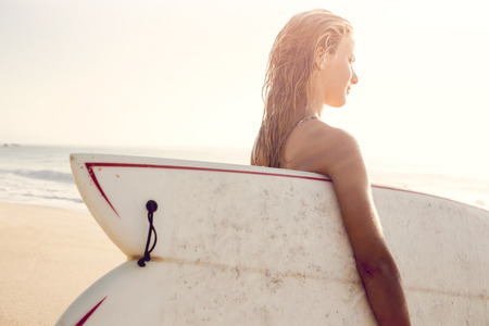 Beautiful young woman holding her surfboard after a day of surf