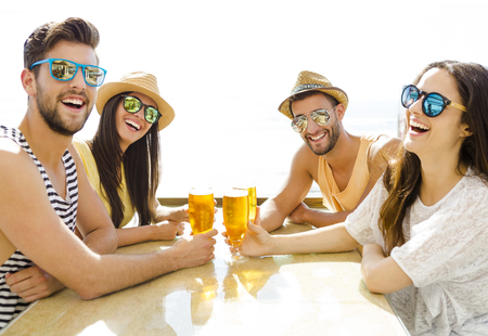 Friends having fun and drinking a cold beer at the beach barの写真素材