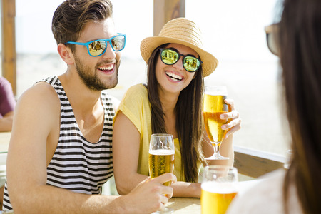 Friends having fun and drinking a cold beer at the beach barの写真素材