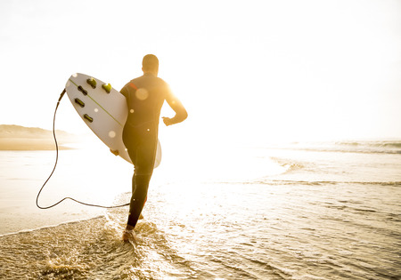 A surfer with his surfboard running to the wavesの写真素材