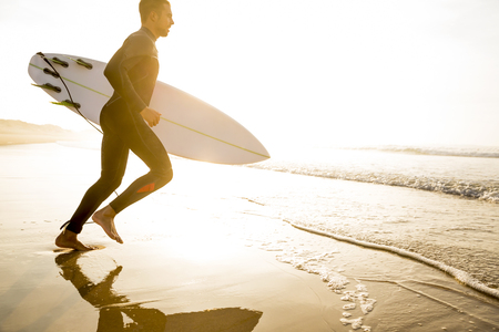 A surfer with his surfboard running to the wavesの写真素材