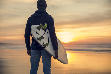 A surfer with his surfboard at the sunset looking to the waves