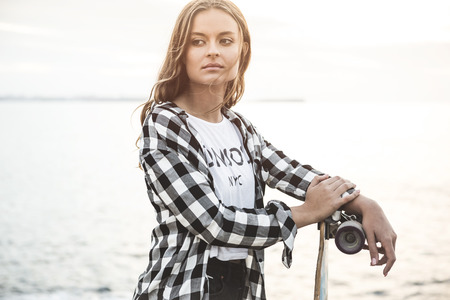 Beautiful and fashion young woman posing at the sunset with a skateboardの写真素材