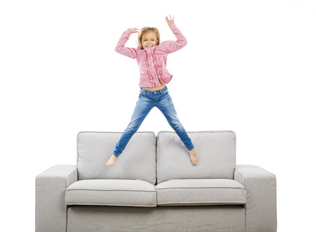 Cute blonde girl jumping over the sofaの写真素材