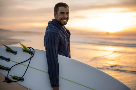 A surfer with his surfboard at the sunset looking to the wavesの写真素材