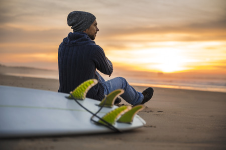 A surfer with his surfboard at the sunset looking to the waves