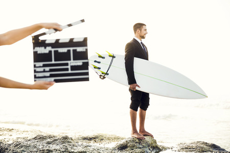 Businessman in front of a clapboard holding is surfboard. Concept about a man starting a new life.の写真素材