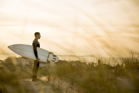 A surfer with his surfboard at the dunes looking to the wavesの写真素材
