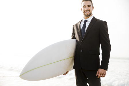 A Businessman holding is surfboard after a long day of workの写真素材