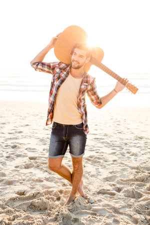 Portrait of a handsome young man with his guitar at the beachの写真素材