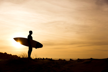 A surfer with his surfboard at the dunes looking to the wavesの写真素材