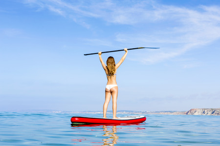A beautiful and happy woman with arms up and learning paddle-surfの写真素材