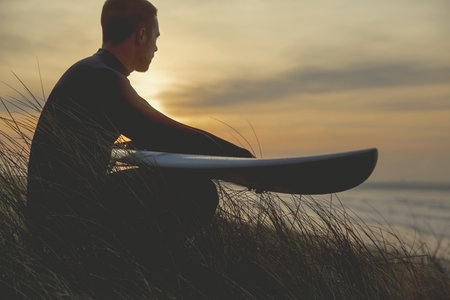 A surfer with his surfboard at the dunes looking to the wavesの写真素材