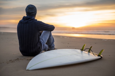 A surfer with his surfboard at the sunset looking to the wavesの写真素材