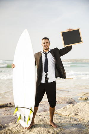 Businessman holding a chalkboard and is surfboard. Concept about a man starting a new life.の写真素材