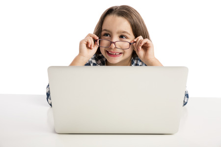 Little girl sitting on a desk and working with a laptop